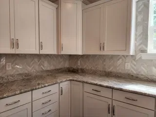 Kitchen with white cabinets, granite countertops and herringbone tile backsplash